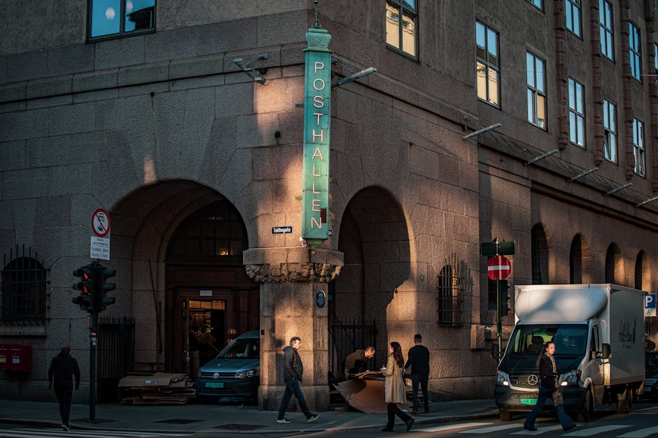 A bustling street scene outside Posthallen in Oslo, Norway, captured at dusk.